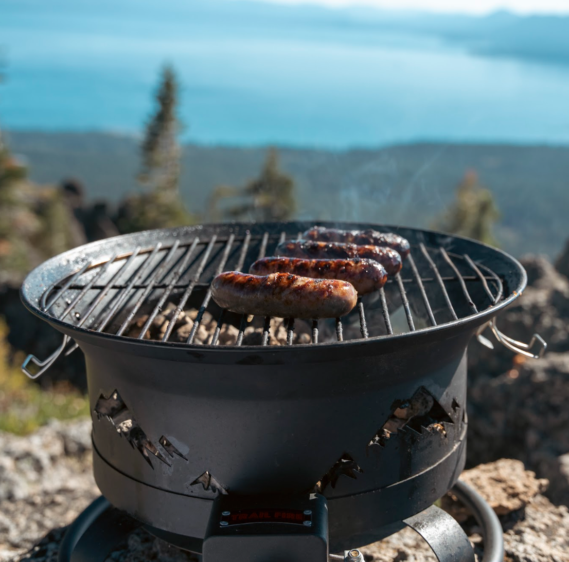 4-in-1 portable propane camping grill shown in bbq mode cooking sausages in the woods
