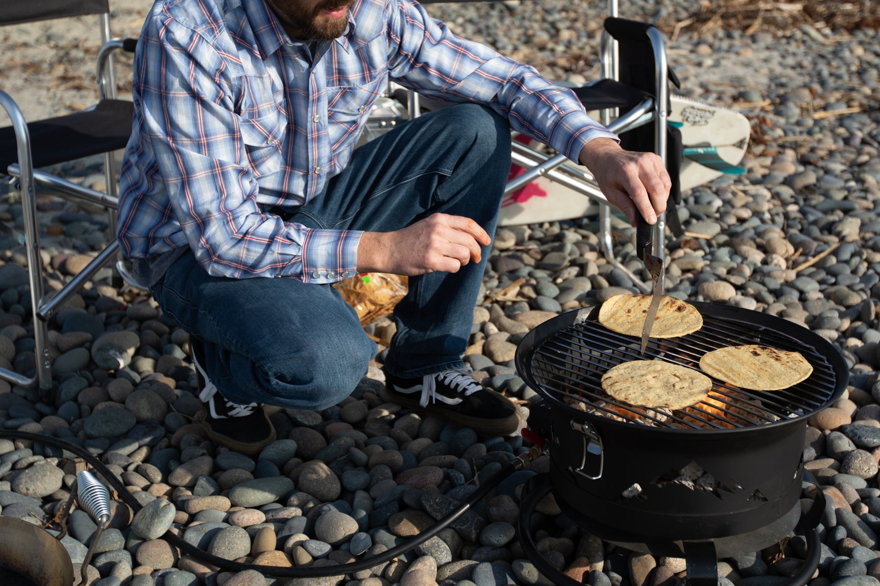 man making tacos heating up tortillas on portable grill at cobblestone beach