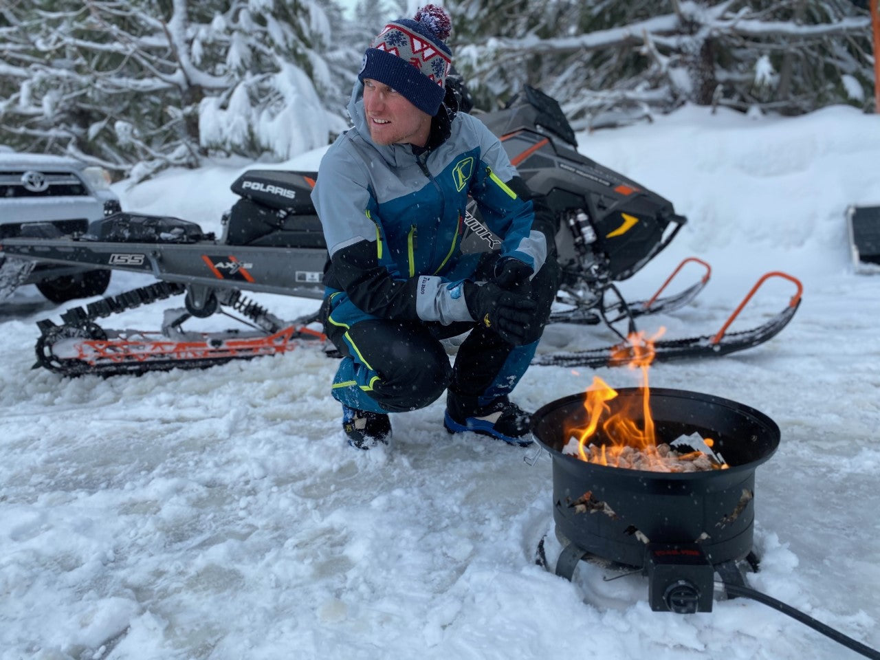 backcountry snowmobiler getting warm with portable grill and fire pit